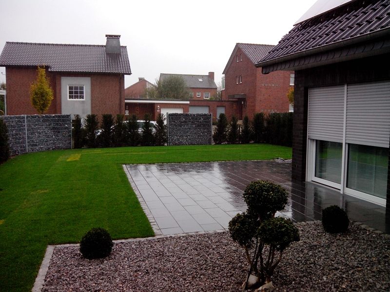 System Gabionensteine -Garten mit Rasen, Kiesfläche und bepflanztem Bereich vor modernen Backsteinhäusern bei bewölktem Himmel