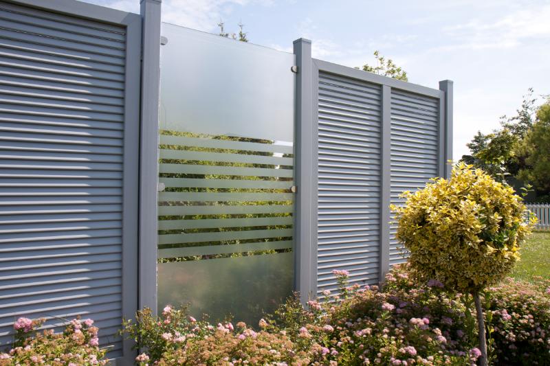 Groja Ambiente Sichtschutz Basicline - Gartenzaun mit grauen Metallpfosten und Sichtschutzpaneelen, darunter ein Teil mit horizontalen Streifen, umgeben von blühenden Sträuchern