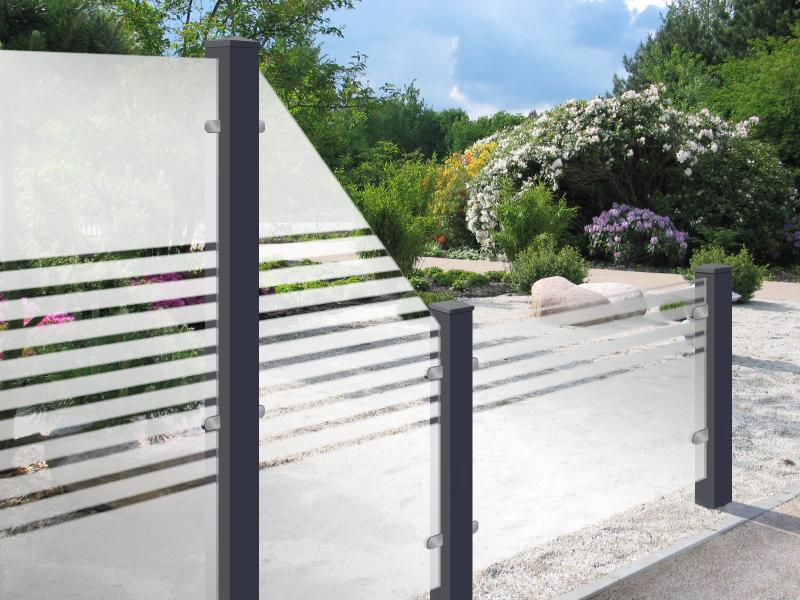 Groja Ambiente streifen - Glaszaun mit horizontalen Streifen und dunklen Pfosten vor einem Garten mit blühenden Sträuchern und Bäumen