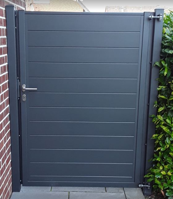Groja Solid - Geschlossene, dunkelgraue Tür mit horizontalen Linien, links Backsteinwand, rechts grüne Hecke