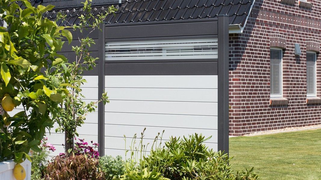 Groja Ambiente - Haus mit weißer Garagentür und rotem Backsteinmauerwerk im Garten mit Büschen