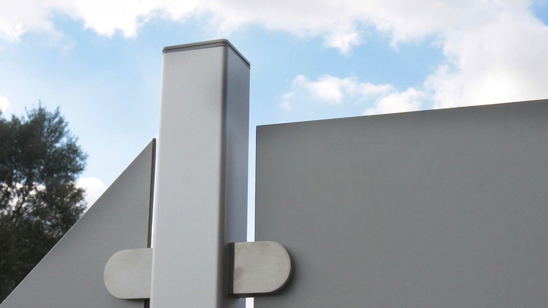 Groja Premo - Nahaufnahme eines grauen Metallzauns mit einem vertikalen Pfosten und einem horizontalen Verbindungselement vor blauem Himmel mit Wolken